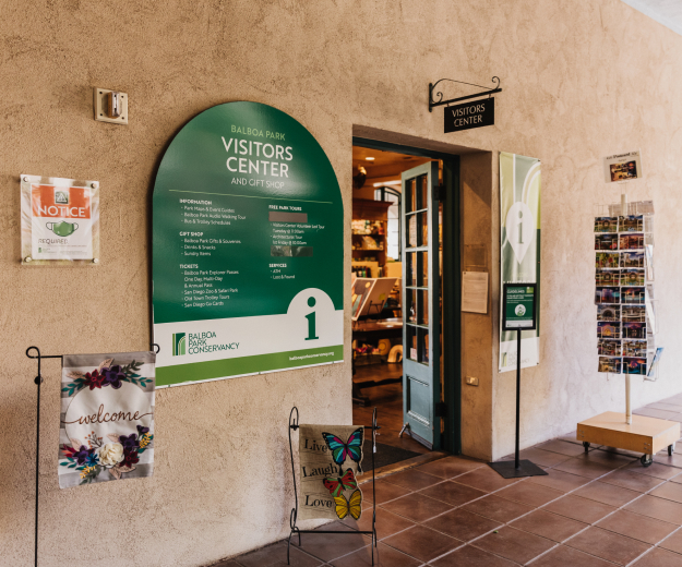 The entry way to the Balboa Park Visitors Center with a green and white arched sign on the left and a display of post cards on the right.