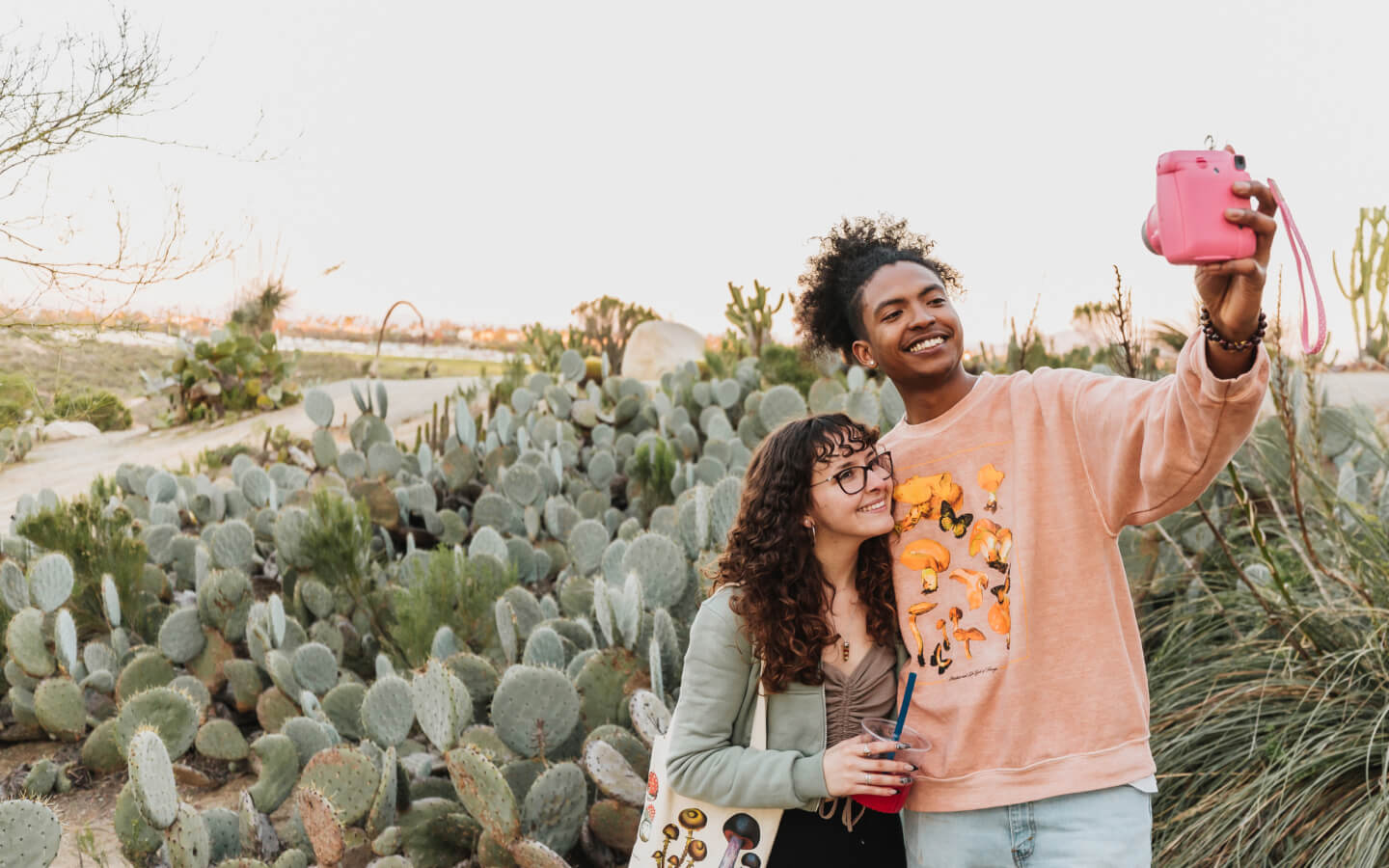 Two people taking a picture with a pink camera in the cactus garden in Balboa Park.