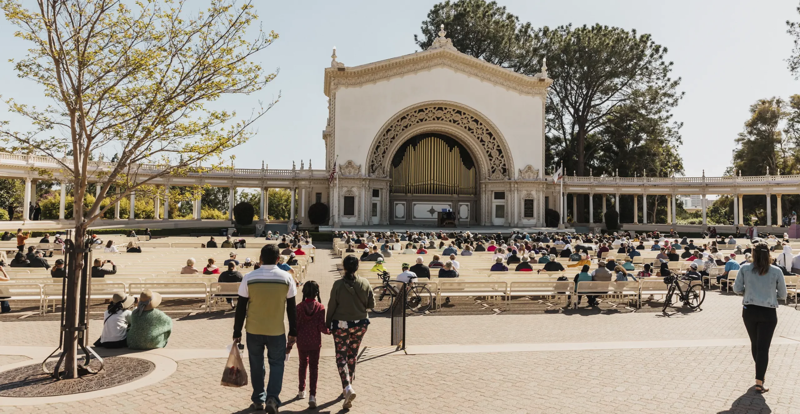 A diverse crowd of people sitting in the stands at the Spreckels Organ Pavilion.