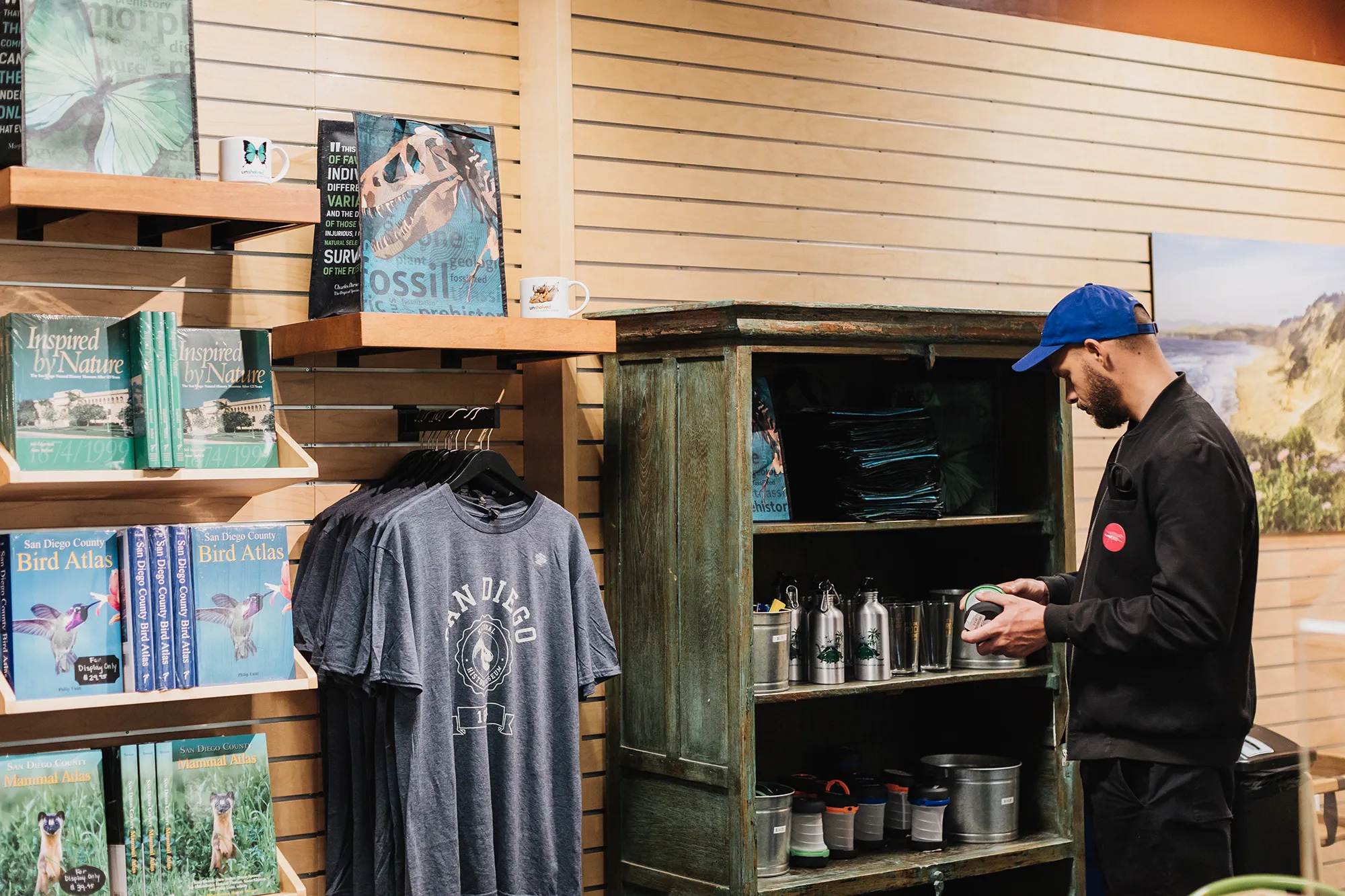 An adult is looking at items for purchase inside theNat shop. Books, shirts, bags, and bottles are on display.