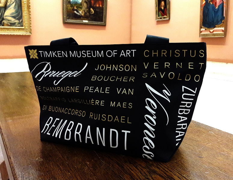 Timken Gift Shop tote bag that is all black with various artist names written on the bag in white and gold.