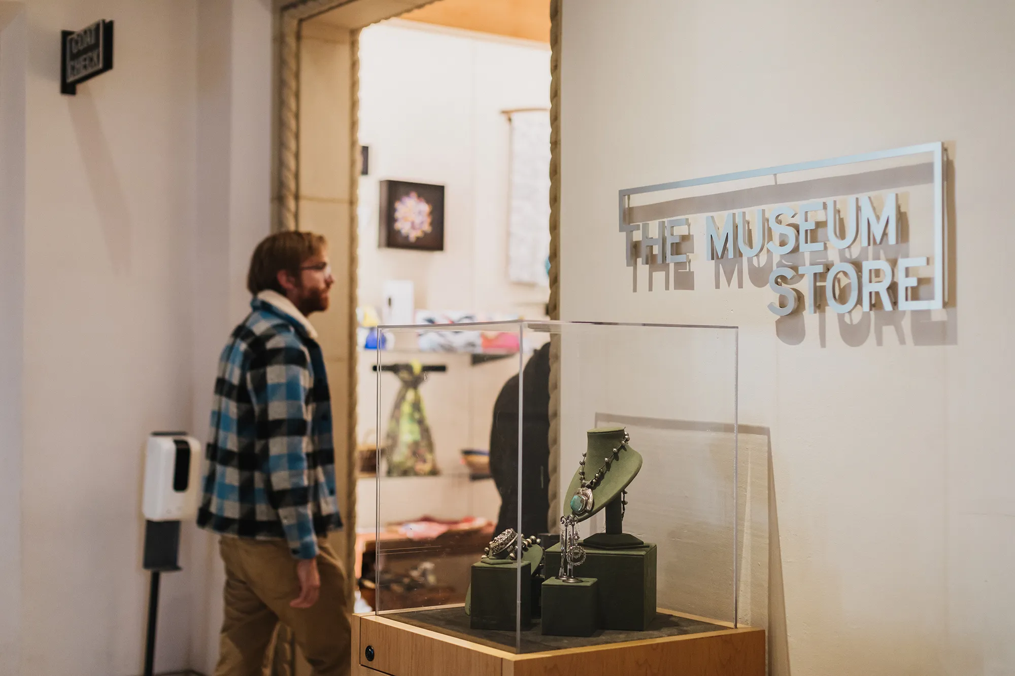 An adult walking through the entrance of the Museum Store at the San Diego Museum of Art. A display of jewelry is located on the right hand side of the entrance.