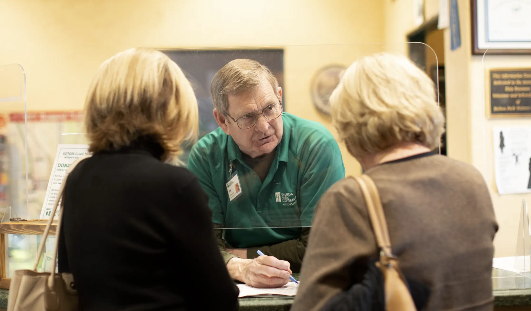 A Visitor Center staff member assisting adult visitors with short blonde hair.