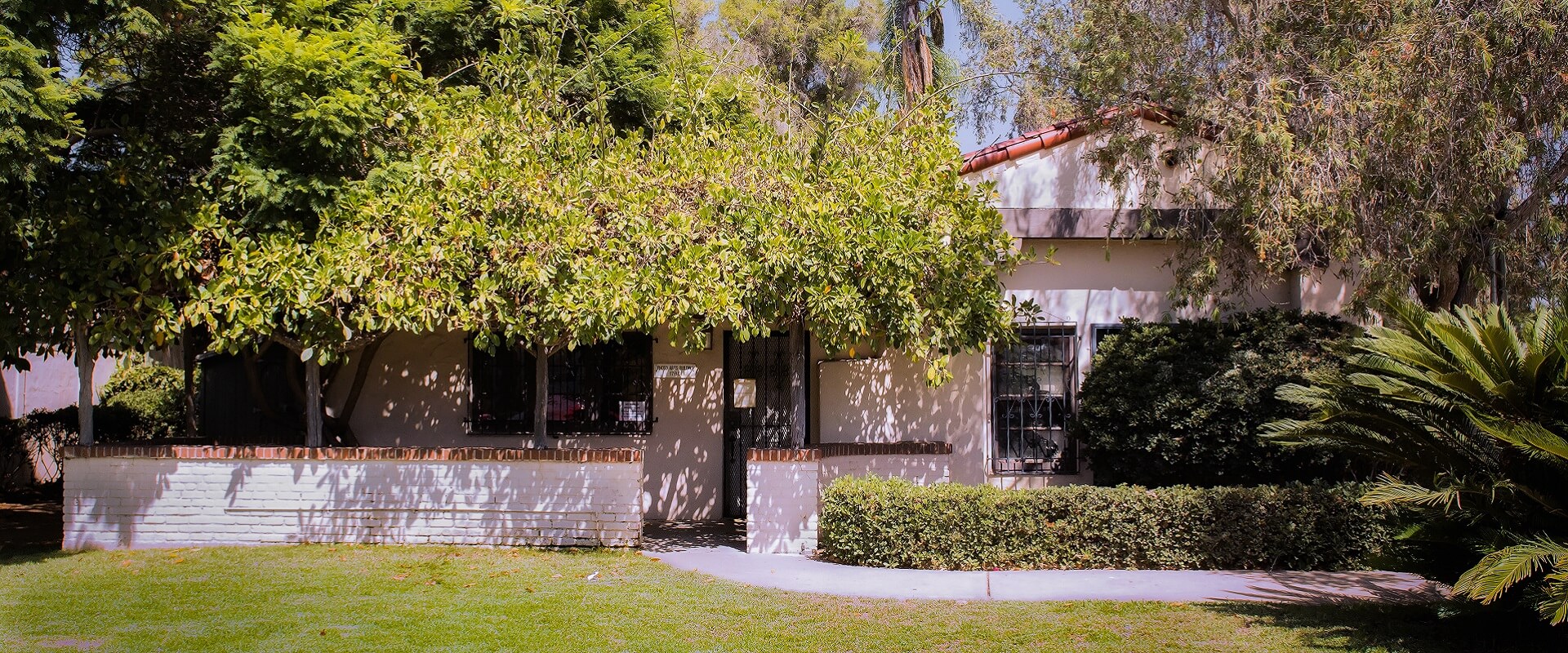 Entrance to the Photographic Arts Building. The building is all white with a red terracotta roof and surrounded by trees and large bushes.