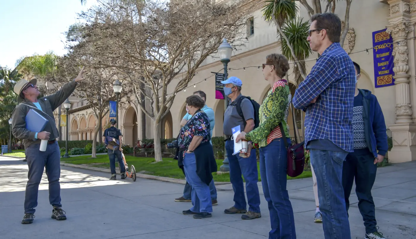 A tour guide mid lecture in front of the House of Hospitality with a group of older adults.