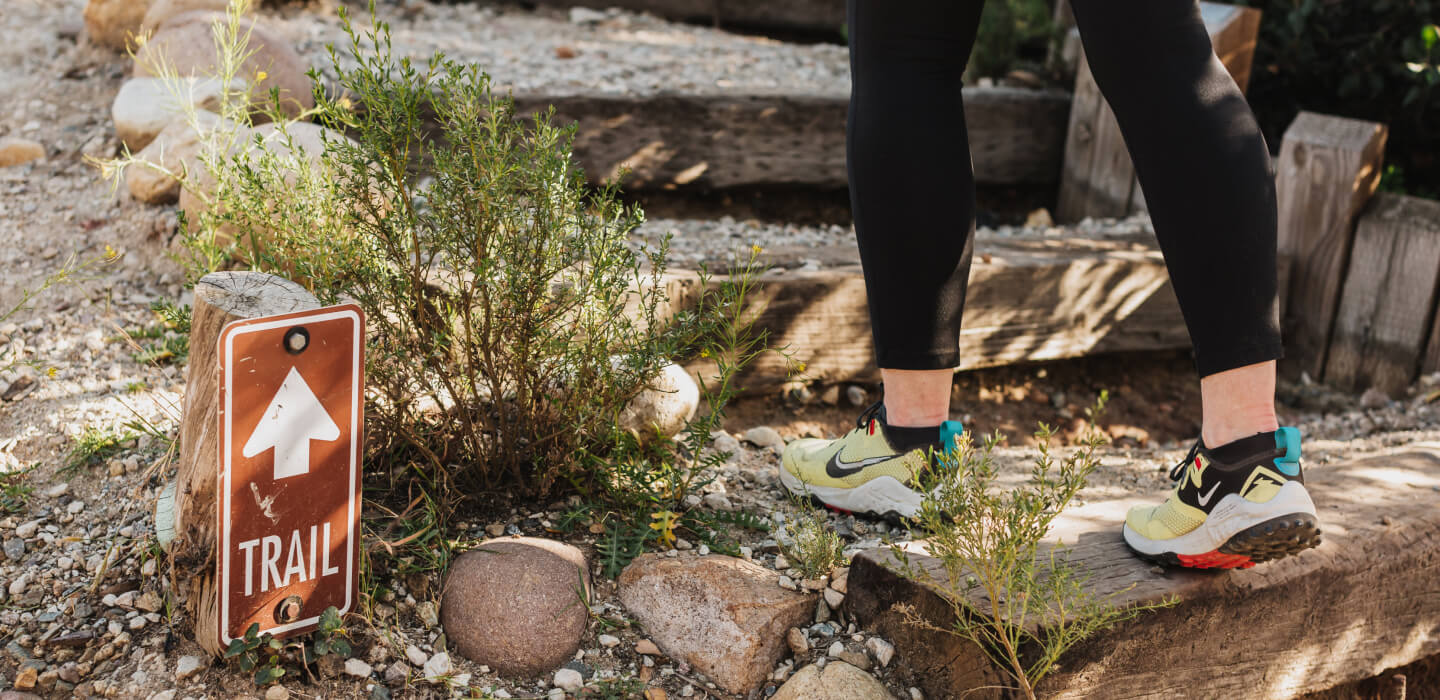 Adult legs wearing brightly colored shoes and black leggings walking up wooden outdoor stairs on a hiking trail.