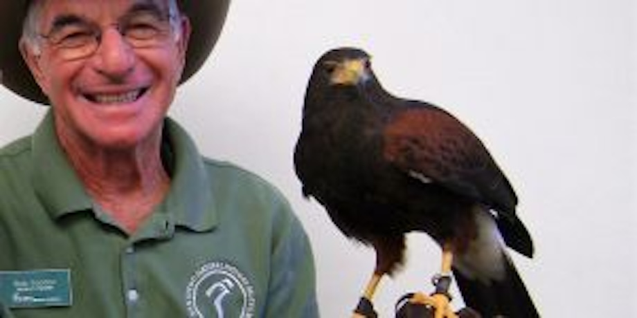 man wearing glasses, a hat and a green shirt holding a brown hawk